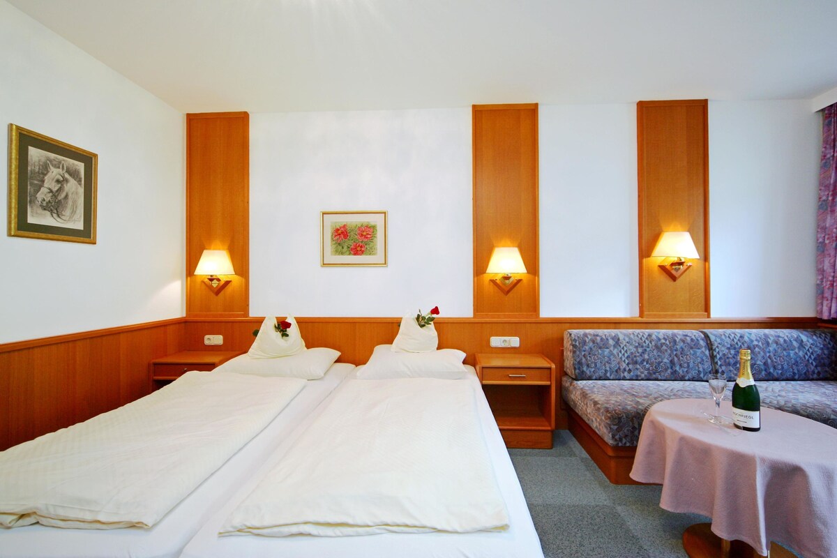 A hotel room with two beds, a sofa, and a table with a bottle of champagne.