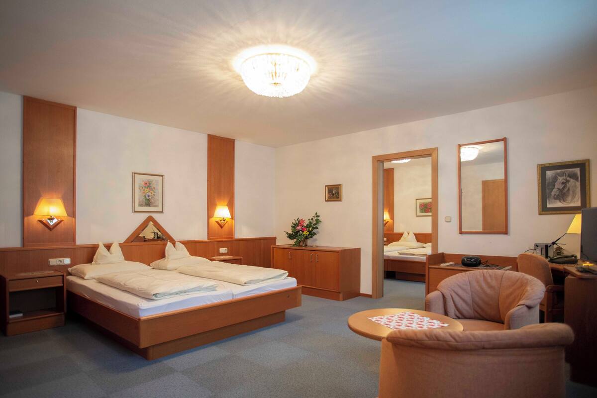 A hotel room with a large bed, bedside tables, a desk, a chair, and a mirror.