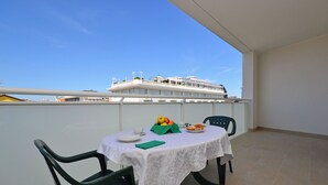 A balcony with a table set for two, chairs, a tablecloth, and a view of a cruise ship. - Equipped apartment for a relaxing stay in Lignano (Lignano Sabbiadoro)