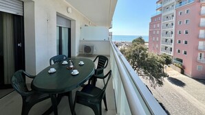 Ein Balkon mit Tisch und Stühlen, einer Klimaanlage und Blick auf das Meer und Gebäude.