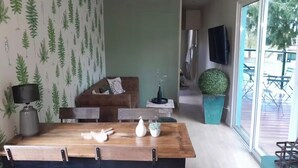 Et spiseområde med et træbord og stole, en sofa og et fjernsyn ophængt på væggen.