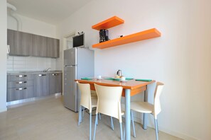 Eine moderne Küche mit Esstisch, Stühlen, einem Kühlschrank und orangefarbenen, schwebenden Regalen.