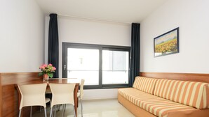 A room with a sofa, dining table, chairs, a window with curtains, and a framed picture on the wall. - Perfect flat to spend a comfortable holiday (Lignano Sabbiadoro)