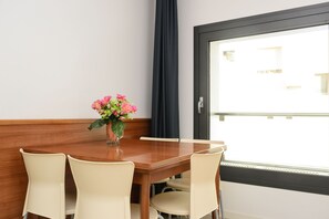Una mesa de comedor con cuatro sillas, un florero con flores y una ventana con vistas a edificios.