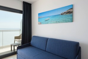 Una habitación moderna con un sofá azul, un cuadro de una escena costera y vistas al mar a través de una ventana.