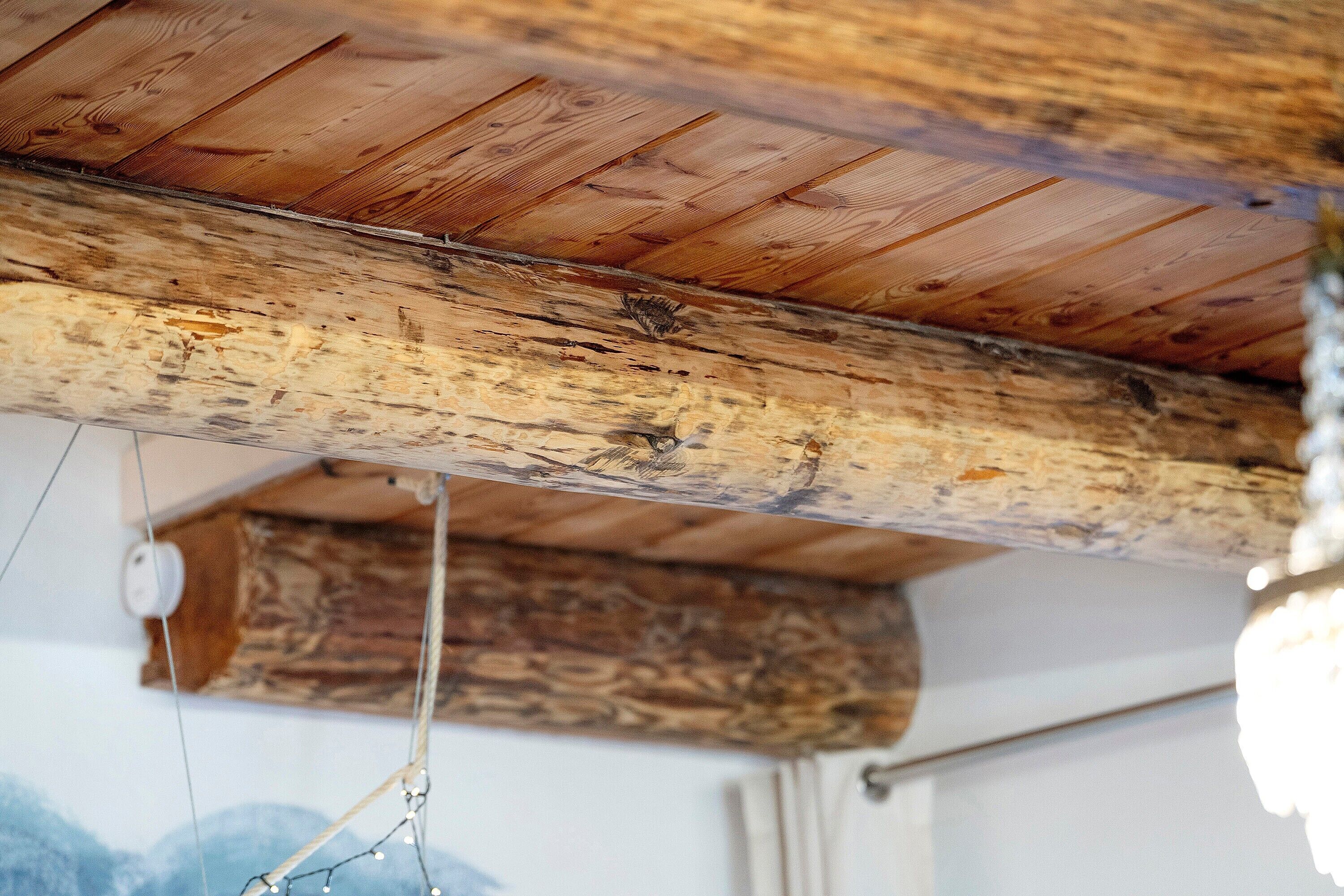 Techo de madera con vigas a la vista, una lámpara colgante y una pared con superficie texturizada.