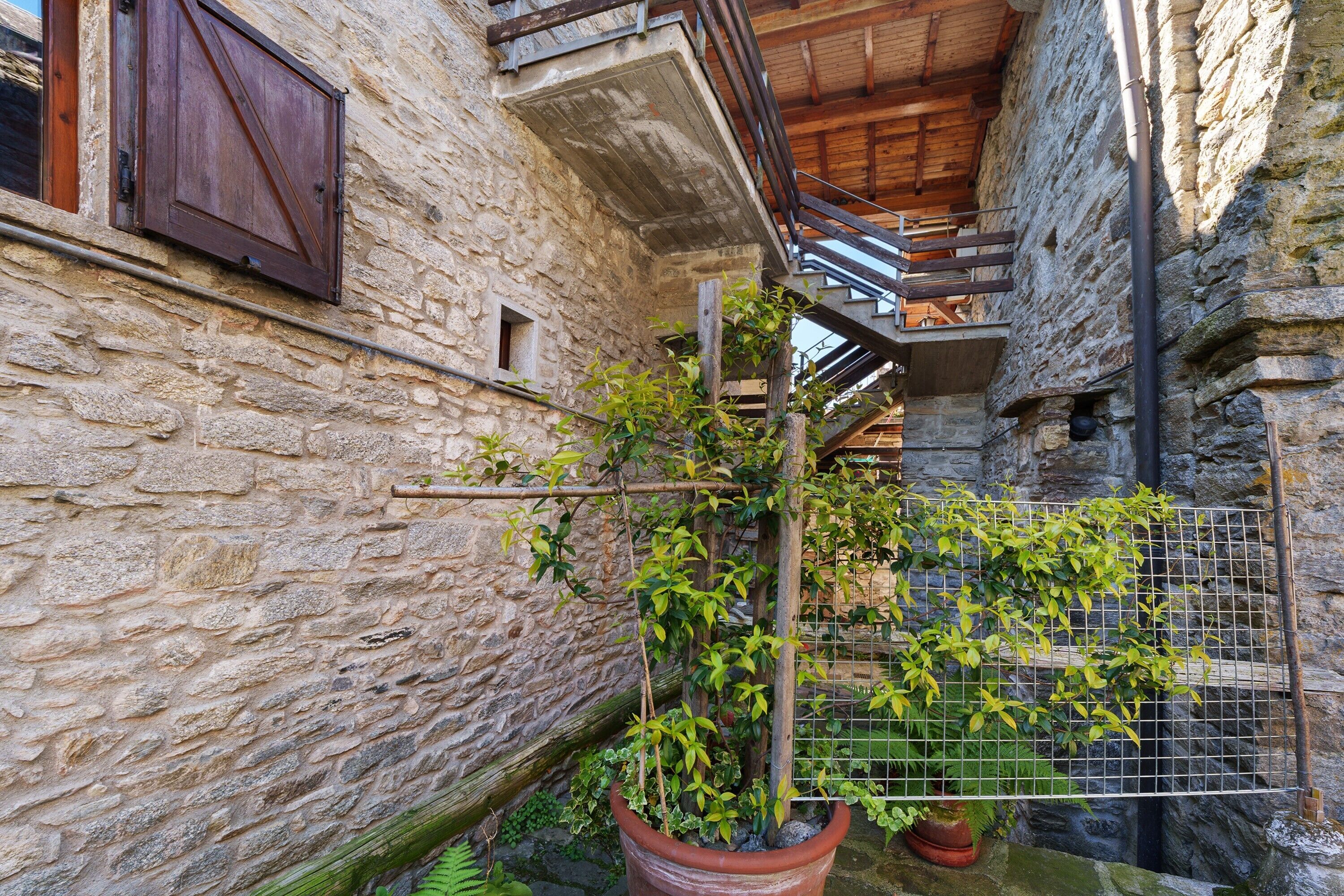 Ein Gebäude aus Stein mit einem hölzernen Balkon, einem Blumentopf und einem Metallzaun.