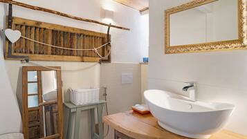 Une salle de bain avec un meuble-lavabo en bois, un lavabo blanc, un miroir avec un cadre doré et un porte-serviettes en bois orné d’un motif en forme de cœur.