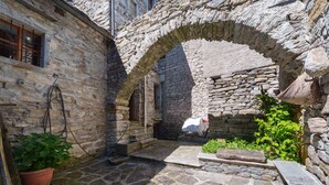 Ein steinerner Innenhof mit einem Bogen, Blumentöpfen und einem mit Stoff bedeckten Gegenstand.