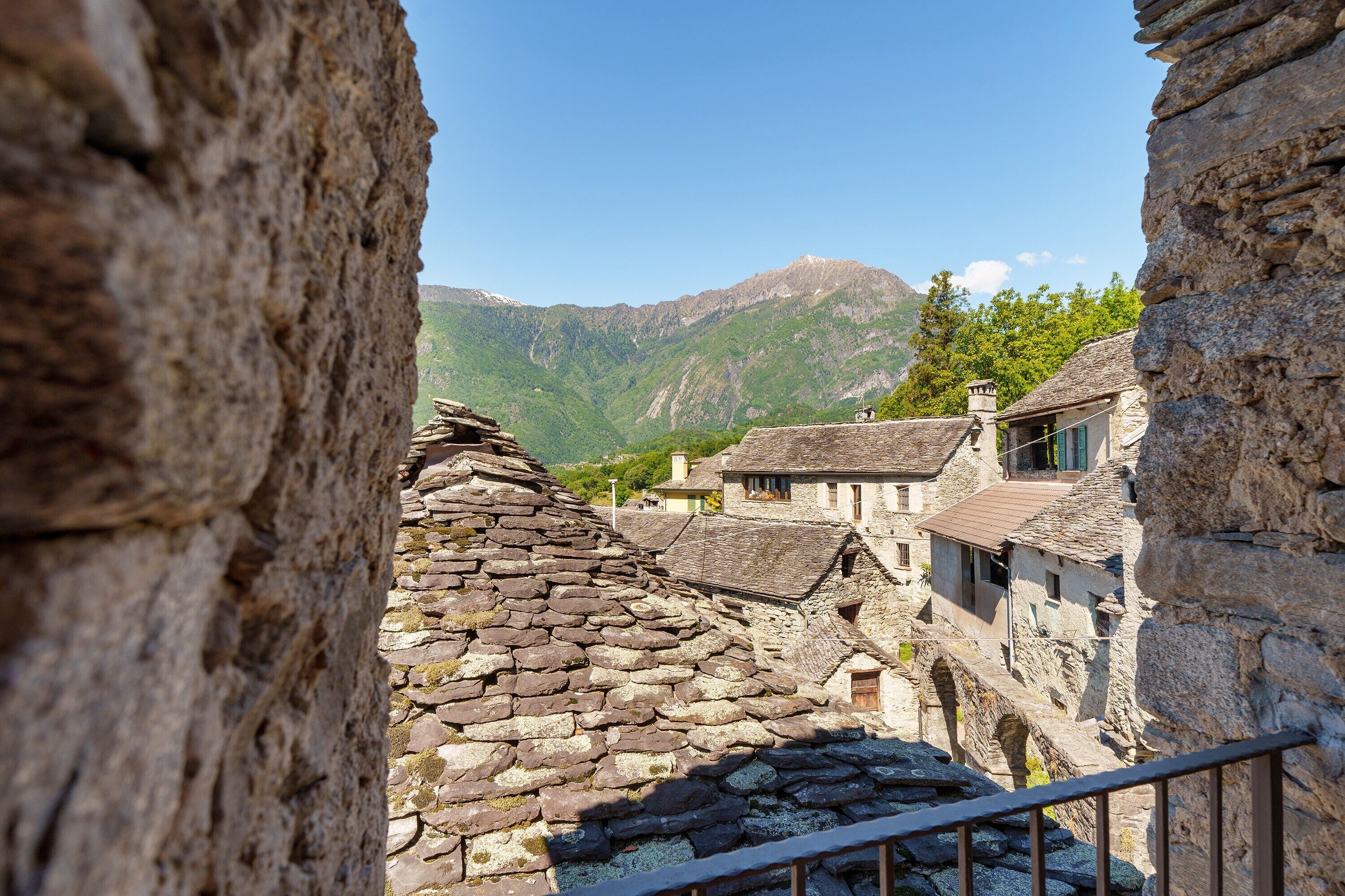 A stone building with a sloped roof, a staircase leading up, and a view of a mountain range in the background.