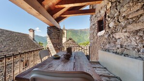 Ein rustikaler Holztisch mit Blick auf ein Steinhaus und Berge im Hintergrund.