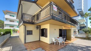 A two-story building with a balcony, a tiled patio, and a sign indicating a rental property. - Lignano flat steps from the beach (Lignano Sabbiadoro)