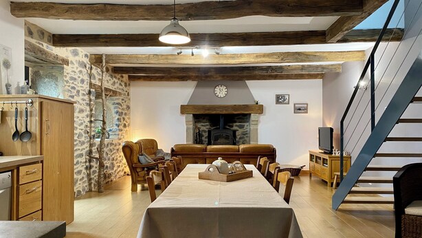 Uma sala de jantar com uma mesa comprida, cadeiras de madeira, uma parede de pedra e uma lareira.