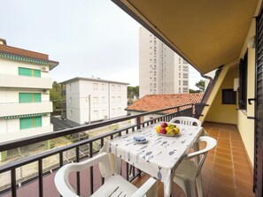 Un balcon avec une table et des chaises, un panier de fruits et une vue sur les immeubles.