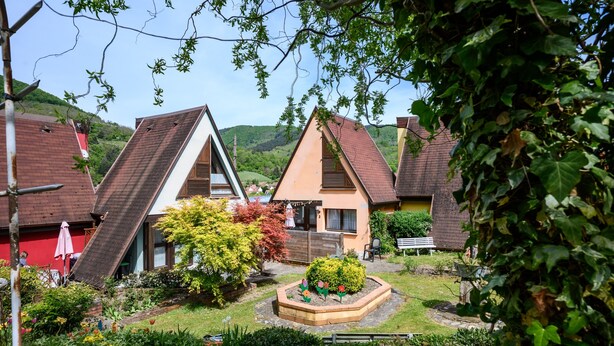 Ein Wohngebiet mit Häusern, einem Garten und einer Hügelkulisse im Hintergrund.