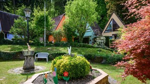 Ein Garten mit einem zentralen Blumenbeet, einer Bank und einer Lampe.