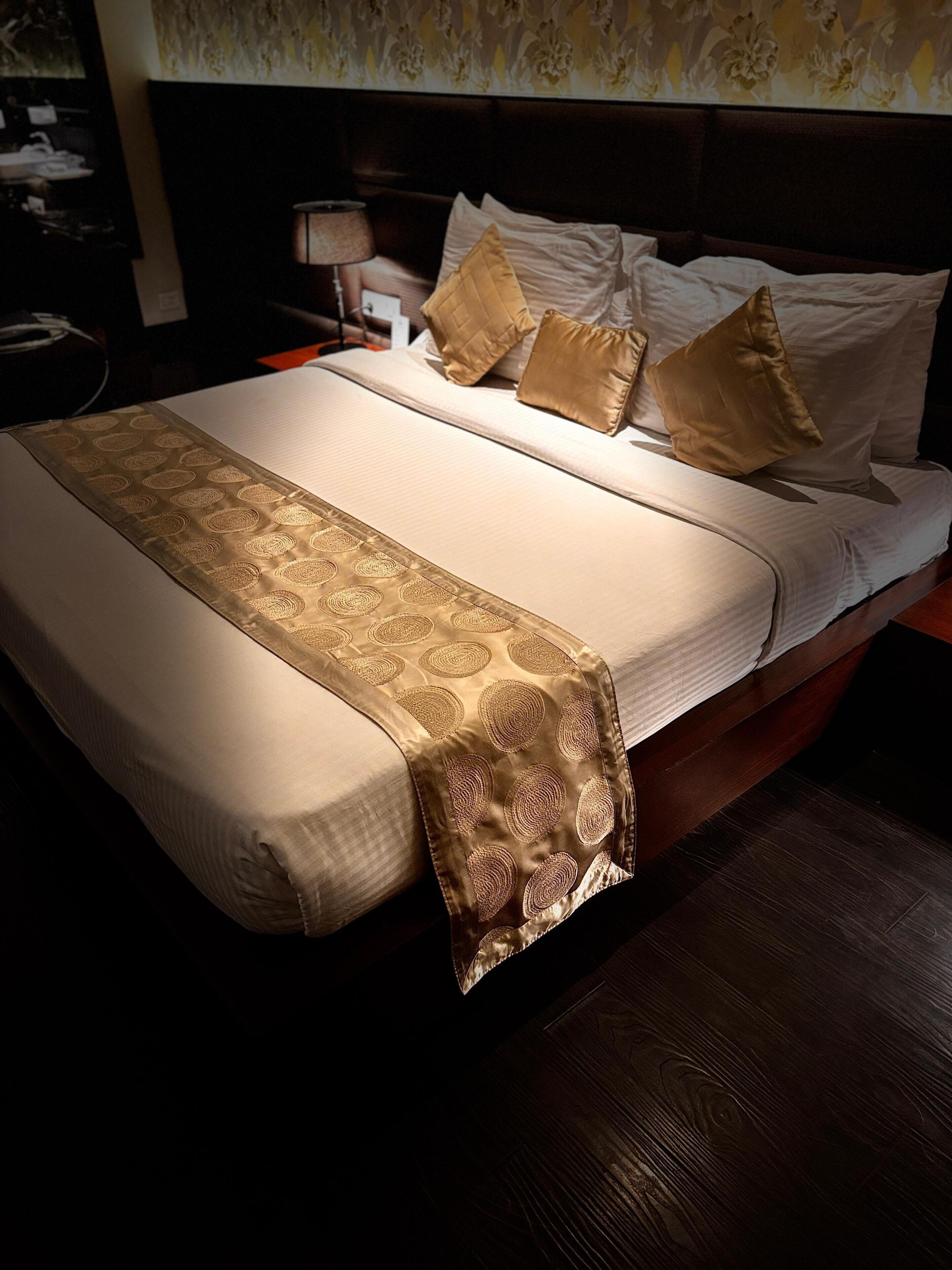 A neatly made bed with a patterned bedspread and pillows, a wooden headboard, and a nightstand with a lamp.