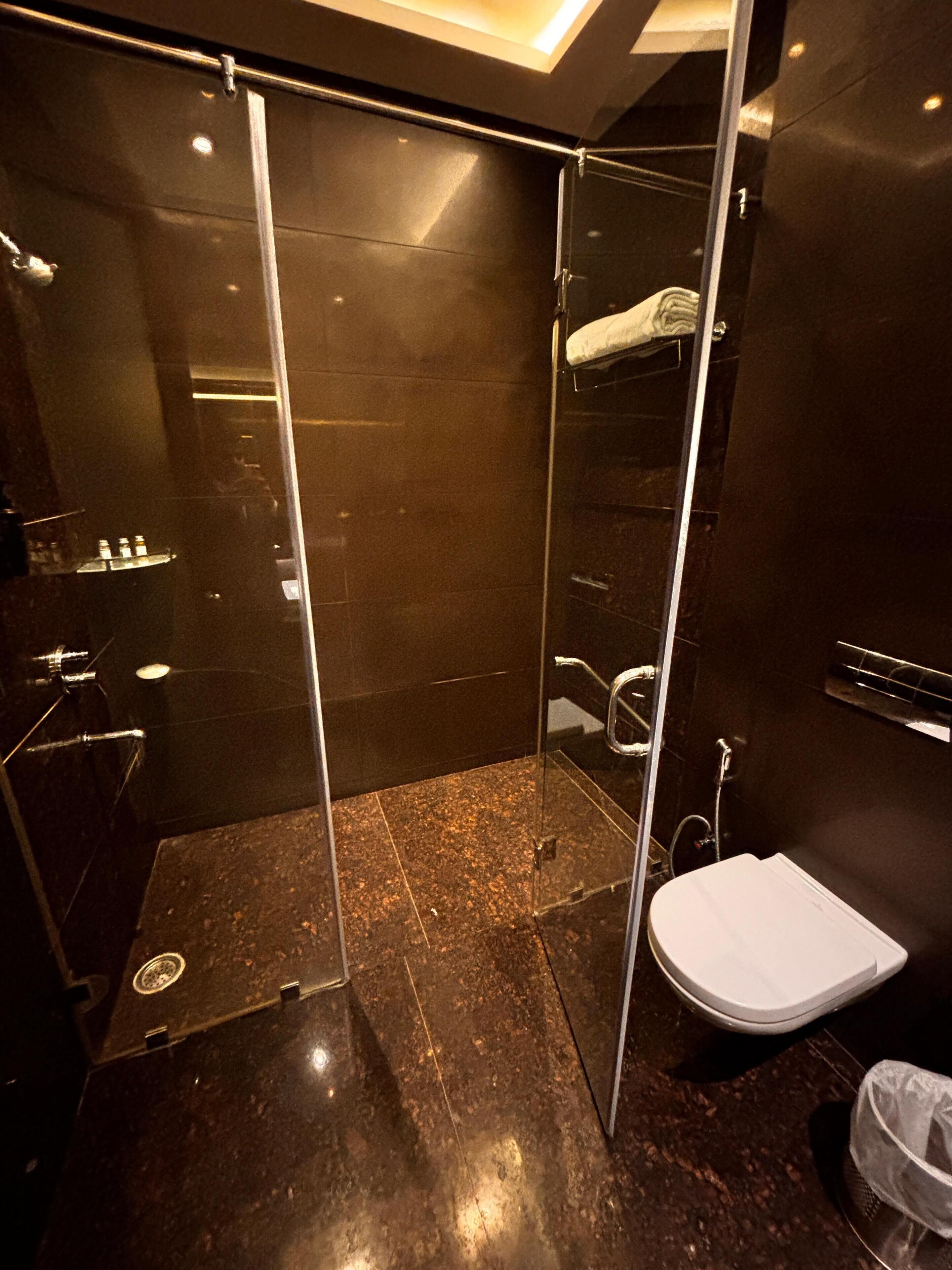 Un baño moderno con cabina de ducha de vidrio, inodoro blanco y piso de baldosas oscuras.