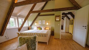 A bedroom with a wooden ceiling, a bed with pillows, a nightstand, and a window. - Unique half-timbered house on a park-like plot with fantastic views (Südheide)