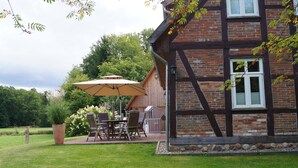A traditional half-timbered house with a patio area featuring a table and chairs, a large umbrella, and a wooden deck. - Unique half-timbered house on a park-like plot with fantastic views (Südheide)