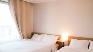 Une chambre d’hôtel avec deux lits, une table de chevet avec une lampe et une fenêtre avec des rideaux.
