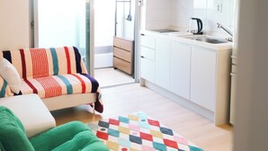 Un salon moderne avec un canapé, un tapis coloré et une vue sur une cuisine dotée de meubles blancs et d’un évier.