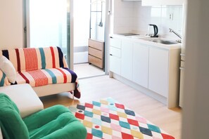Ein modernes Wohnzimmer mit einer Couch, einem farbenfrohen Teppich und Blick in eine Küche mit weißen Schränken und einer Spüle.