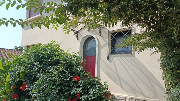 A building with a red door, a window with a metal grille, and a stone wall. - The Trumpets of Jericho (Tartas)