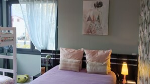A bedroom with a bunk bed, a bedside table with a lamp, a painting on the wall, and a window with curtains. - The Trumpets of Jericho (Tartas)