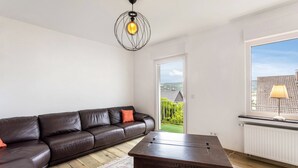 Een woonkamer met een bruine leren bank, een houten salontafel, een kamerbreed tapijt, een hanglamp en uitzicht door een raam.