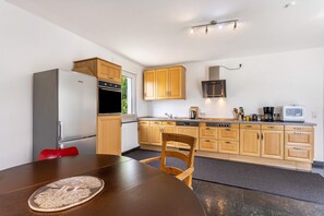 Una cocina moderna con armarios de madera, electrodomésticos de acero inoxidable y una zona de comedor con una mesa y una silla.