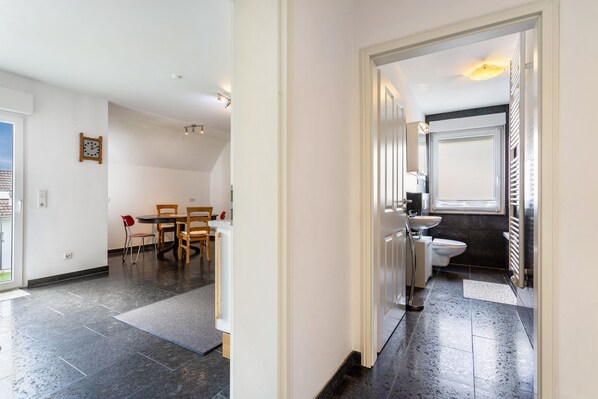 A modern interior with a dining area, a bathroom with a toilet and sink, and a hallway leading to another room.
