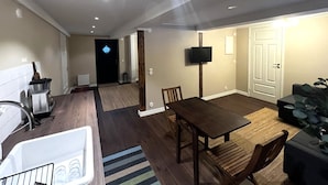 Een moderne woonkamer met een eettafel, een bank, een aan de muur bevestigde televisie en een keuken met een blender en een koelkast.