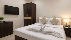 A hotel room with a bed, a TV mounted on the wall, a wardrobe, and a bedside table with a lamp.