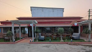 A building with a red roof, a covered patio area with tables and chairs, and a large window.