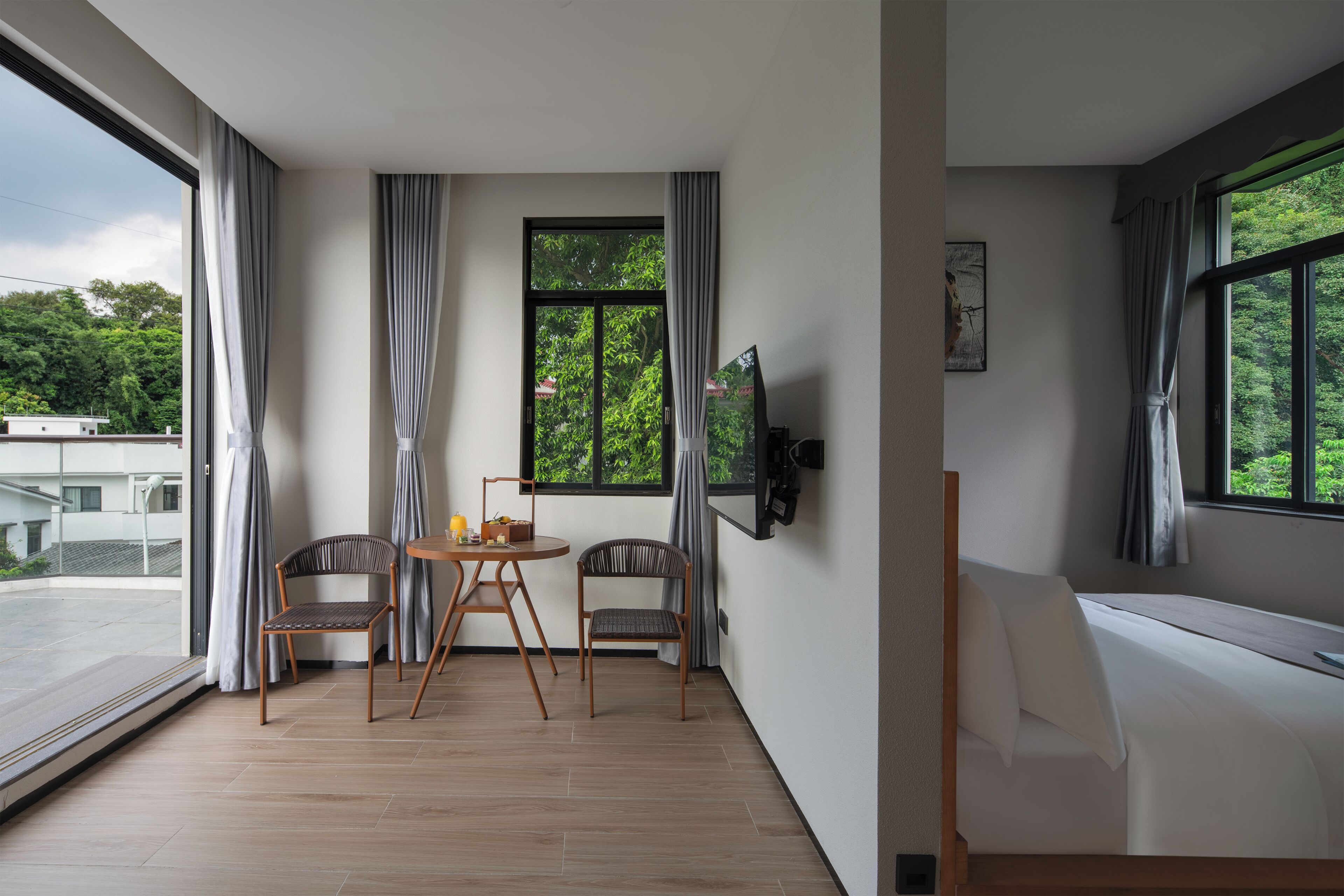 A modern room with a large window, a bed, a TV, and a dining area with chairs and a table.