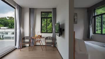 A modern room with a large window, a bed, a TV, and a dining area with chairs and a table.