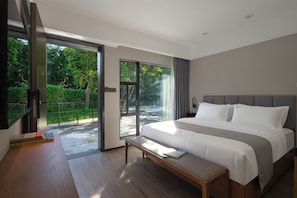 Una habitación de hotel moderna con una cama grande, un banco, una zona de lectura y un ventanal corredero que da a un espacio exterior.