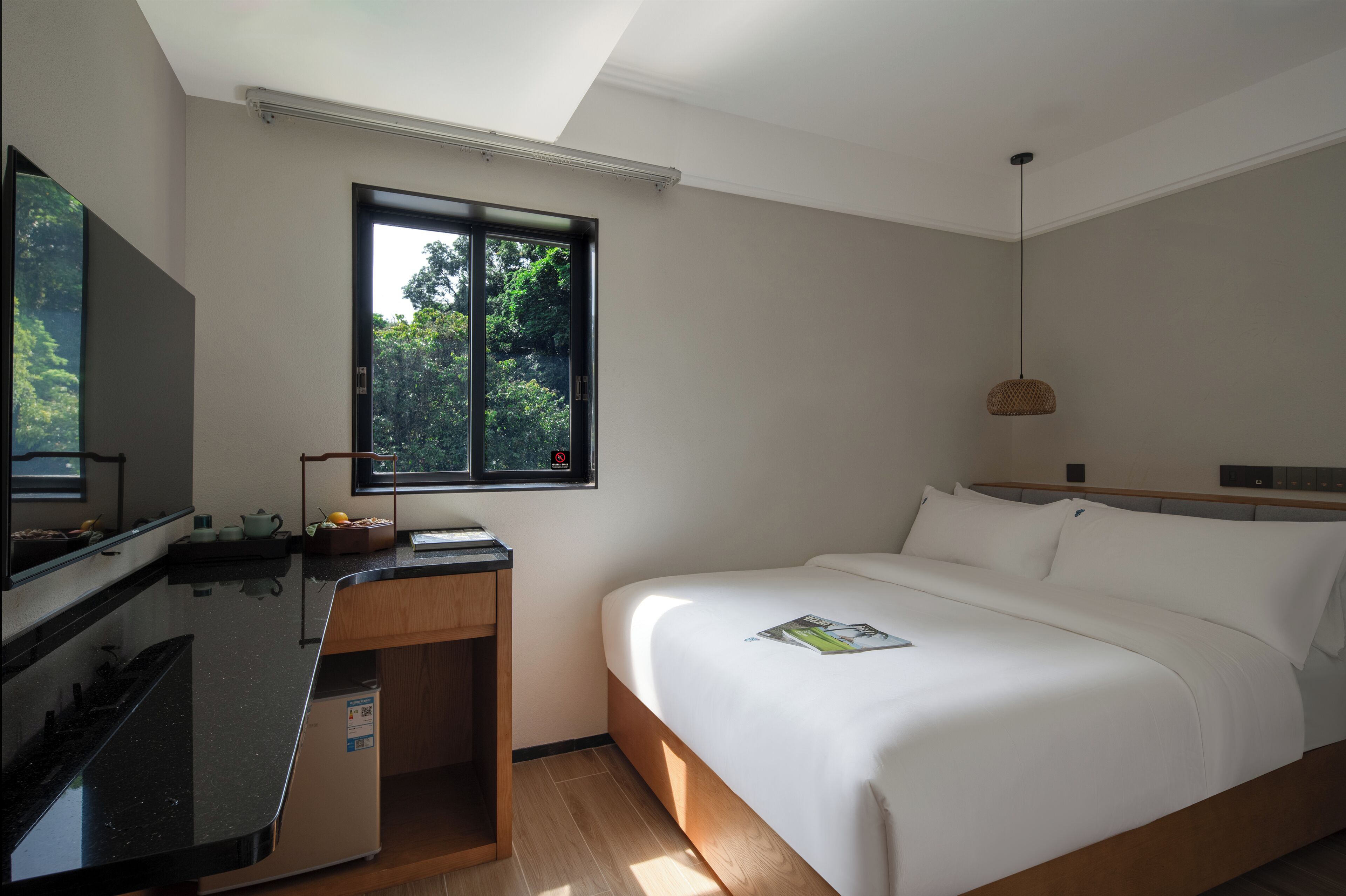 A hotel room with a bed, a desk, a television, and a window with a view of trees.