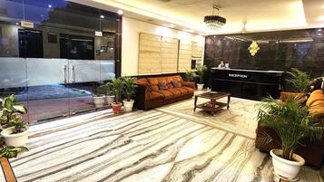 A modern reception area with a marble floor, a reception desk, a brown sofa, and potted plants.