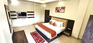 A hotel room with a bed, a TV, a wardrobe, and a red patterned rug. - RoadRolls (Varanasi)