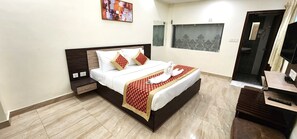 A hotel room with a bed, a TV, a desk, and a bathroom visible through a window. - RoadRolls (Varanasi)