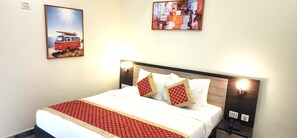 A hotel room with a bed, two wall-mounted lamps, a telephone, and two paintings. - RoadRolls (Varanasi)