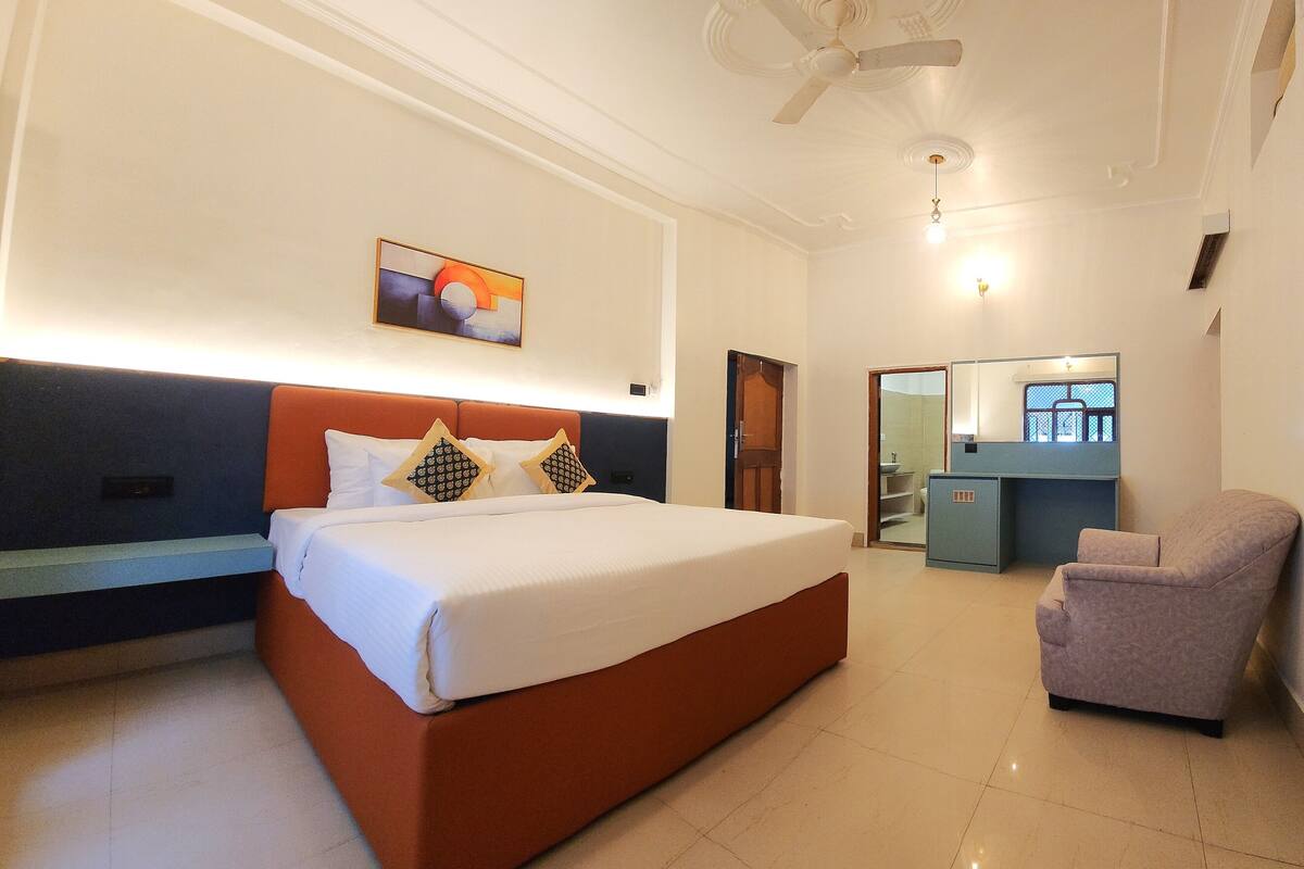 A hotel room with a large bed, a chair, a desk, a ceiling fan, and a painting on the wall.