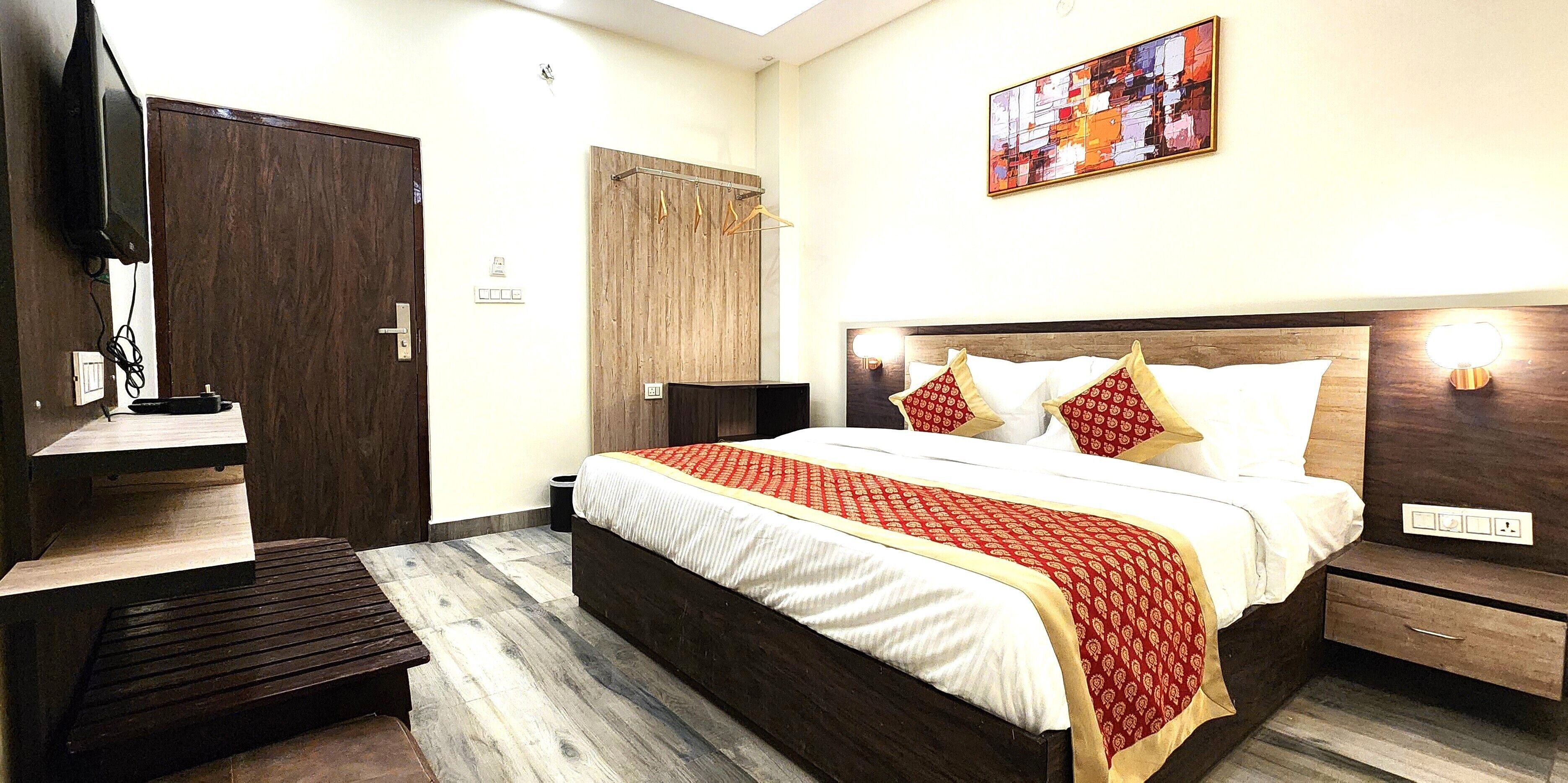 A hotel room with a bed, bedside tables, a wardrobe, a TV, and a painting on the wall.