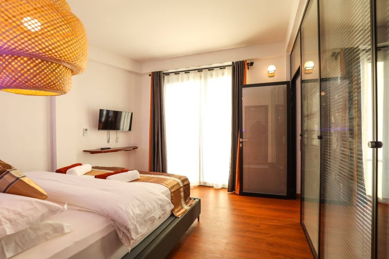 A hotel room with two beds, a television, a large window with curtains, and a sliding glass door.