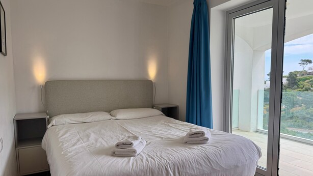A bedroom with a bed, bedside tables, a curtain, and a view through a glass door. - Fantastic Villa with Pool and Stunning Sea Views (Begur)