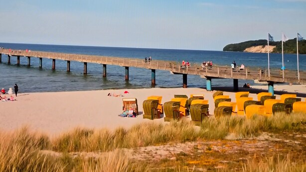 Une plage avec une jetée qui s’avance dans l’eau, des rangées de chaises de plage et une zone sablonne où se trouvent des gens.