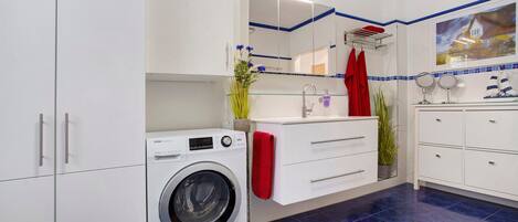 A modern bathroom with a washing machine, a glass sink, and a mirror.