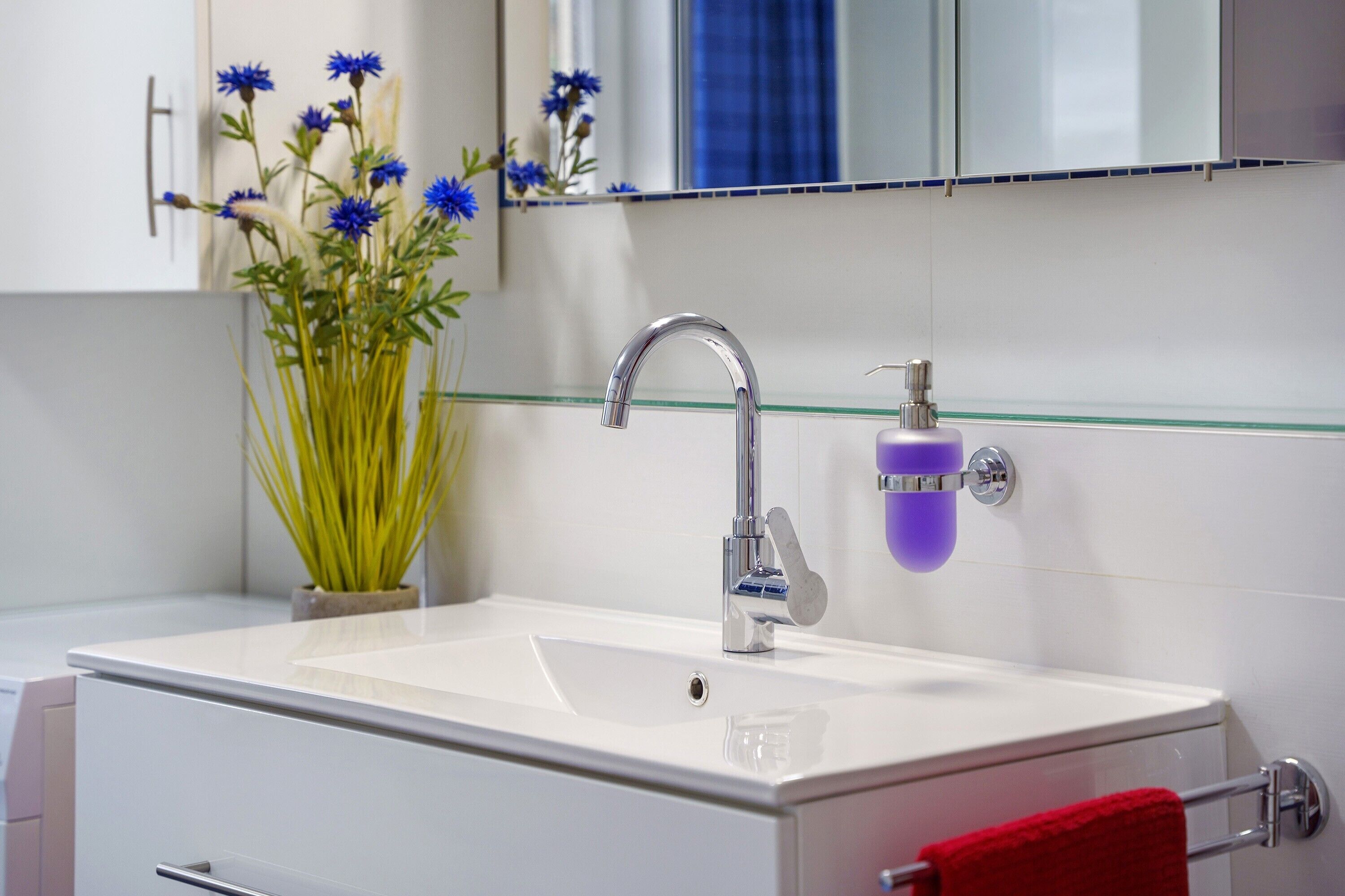 A bathroom with a white sink, chrome faucet, and a glass soap dispenser.